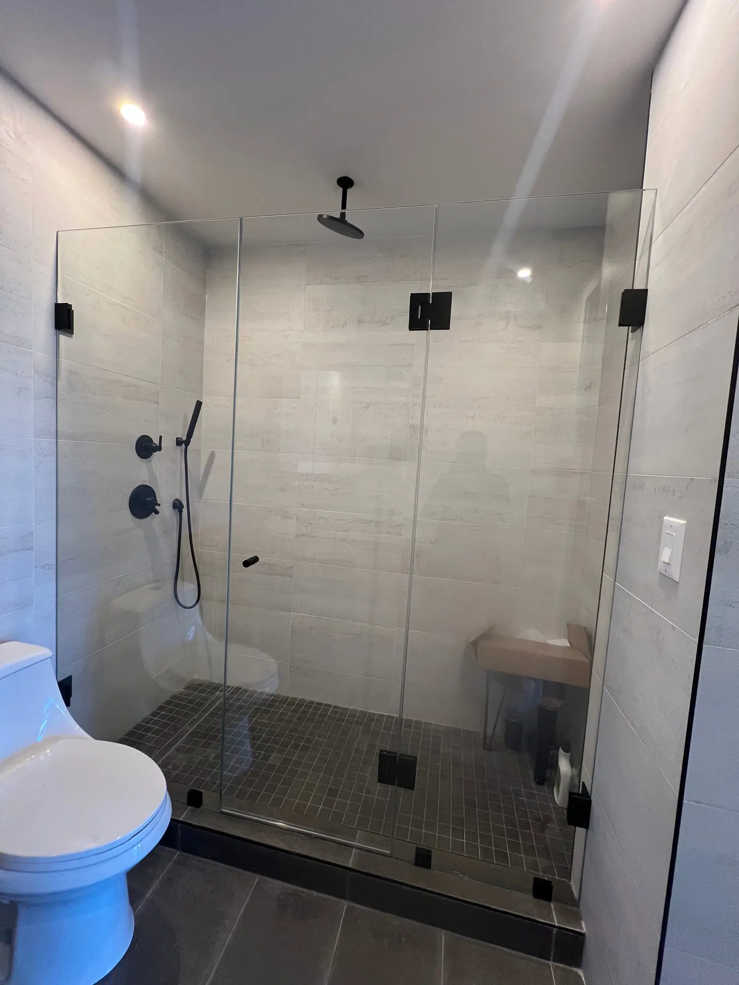 A frameless corner shower with black fittings and a grey mosaic floor in a compact bathroom