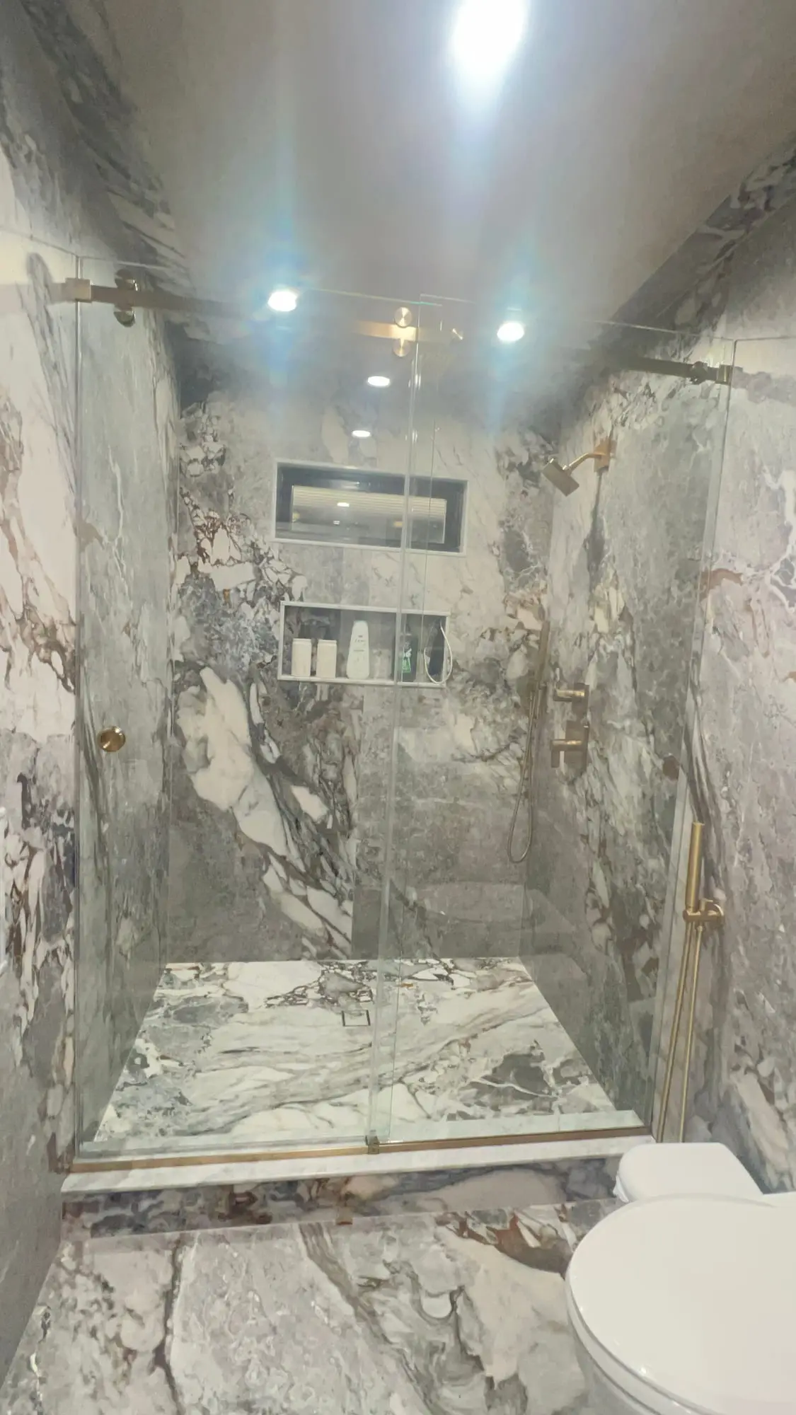 A walk-in shower lined floor to ceiling in heavily veined marble, with a recessed niche and a single frameless glass panel