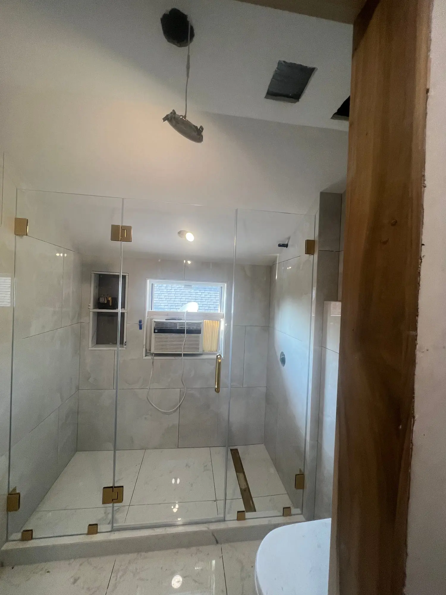 A white marble shower with brass fittings behind a frameless glass panel, with an exposed timber beam overhead