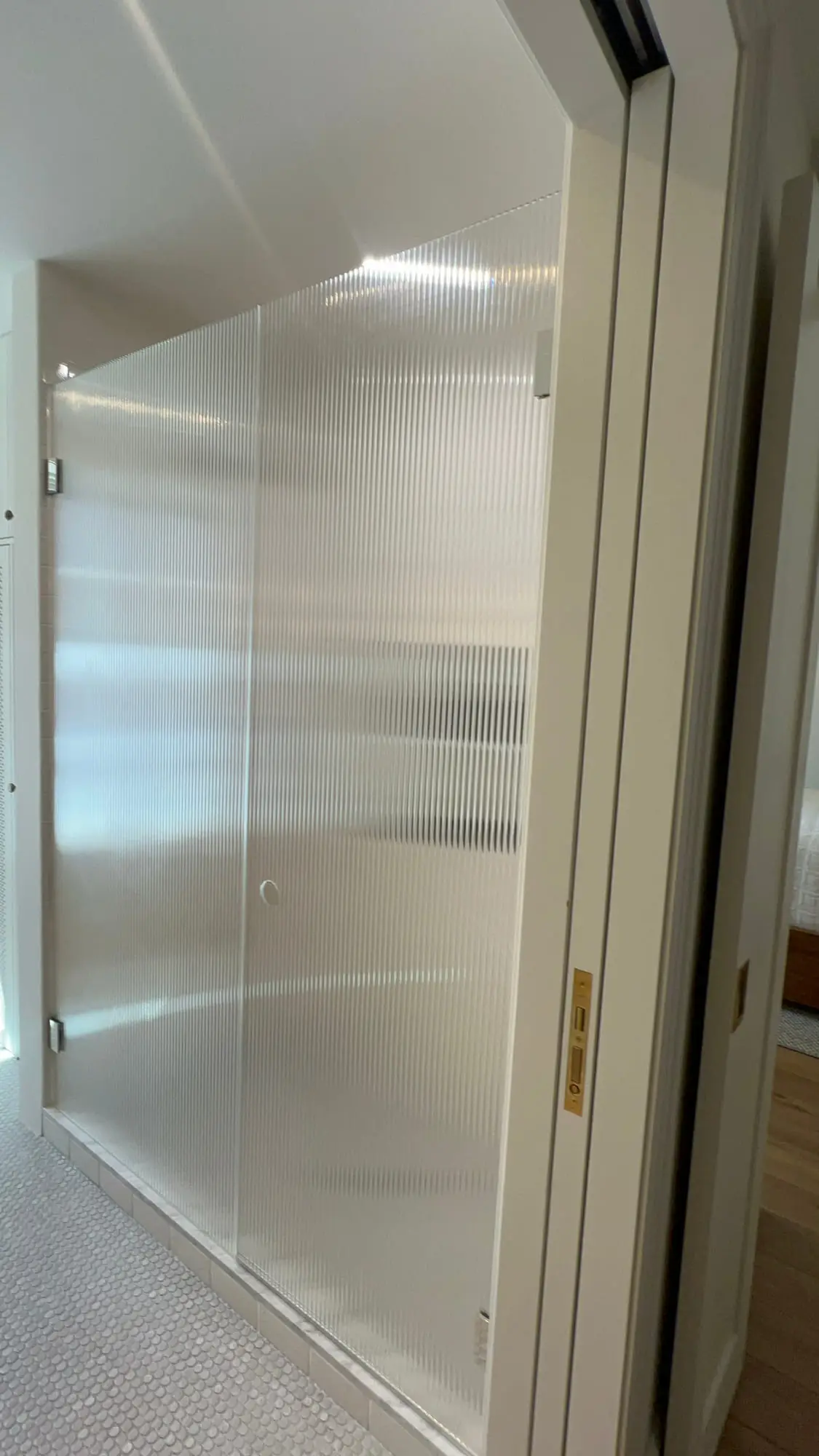 A shower door in textured privacy glass with a slim gold frame edge
