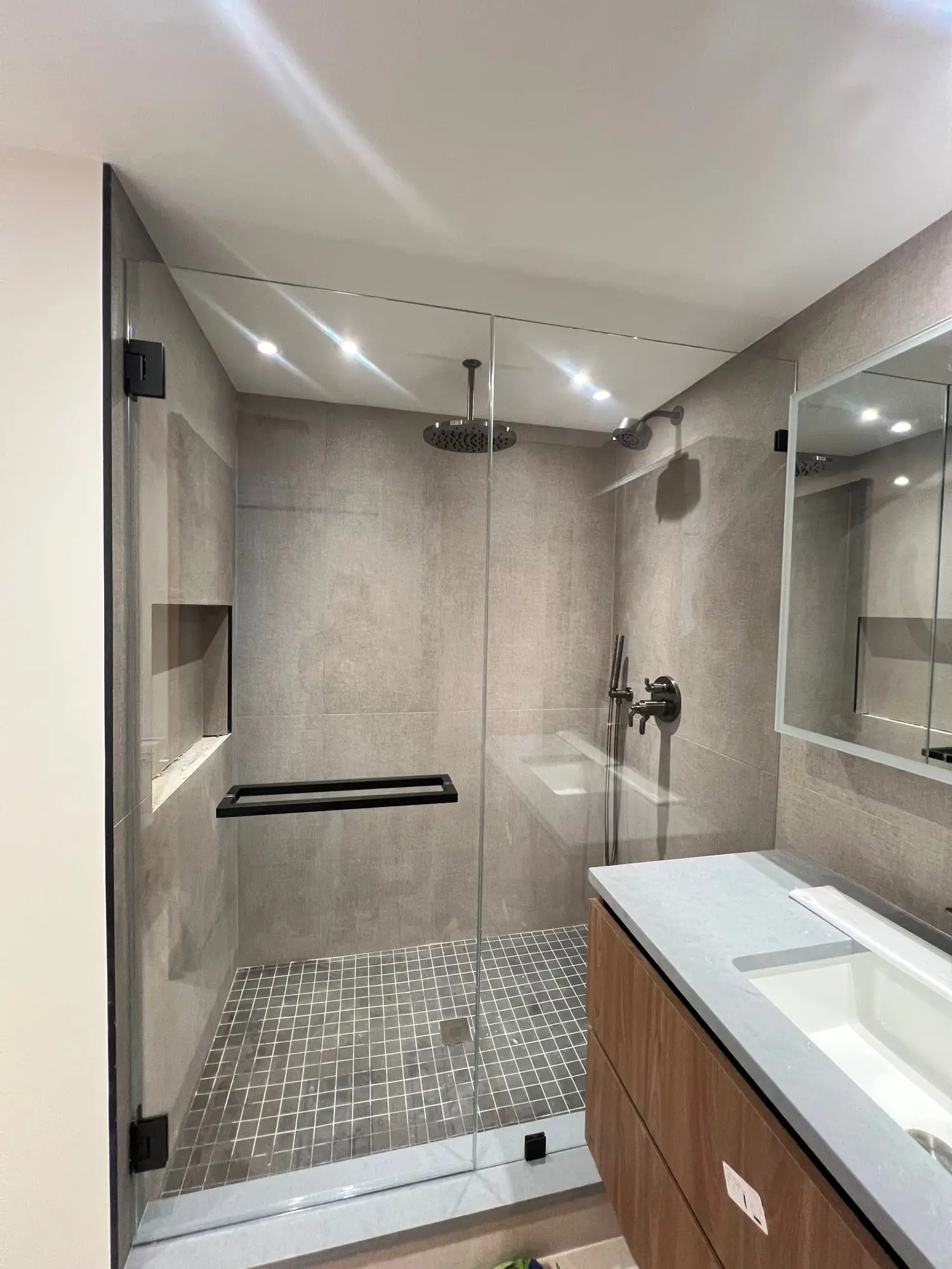 A walk-in shower in large grey tile with black fittings and a built-in niche, opposite a long double vanity