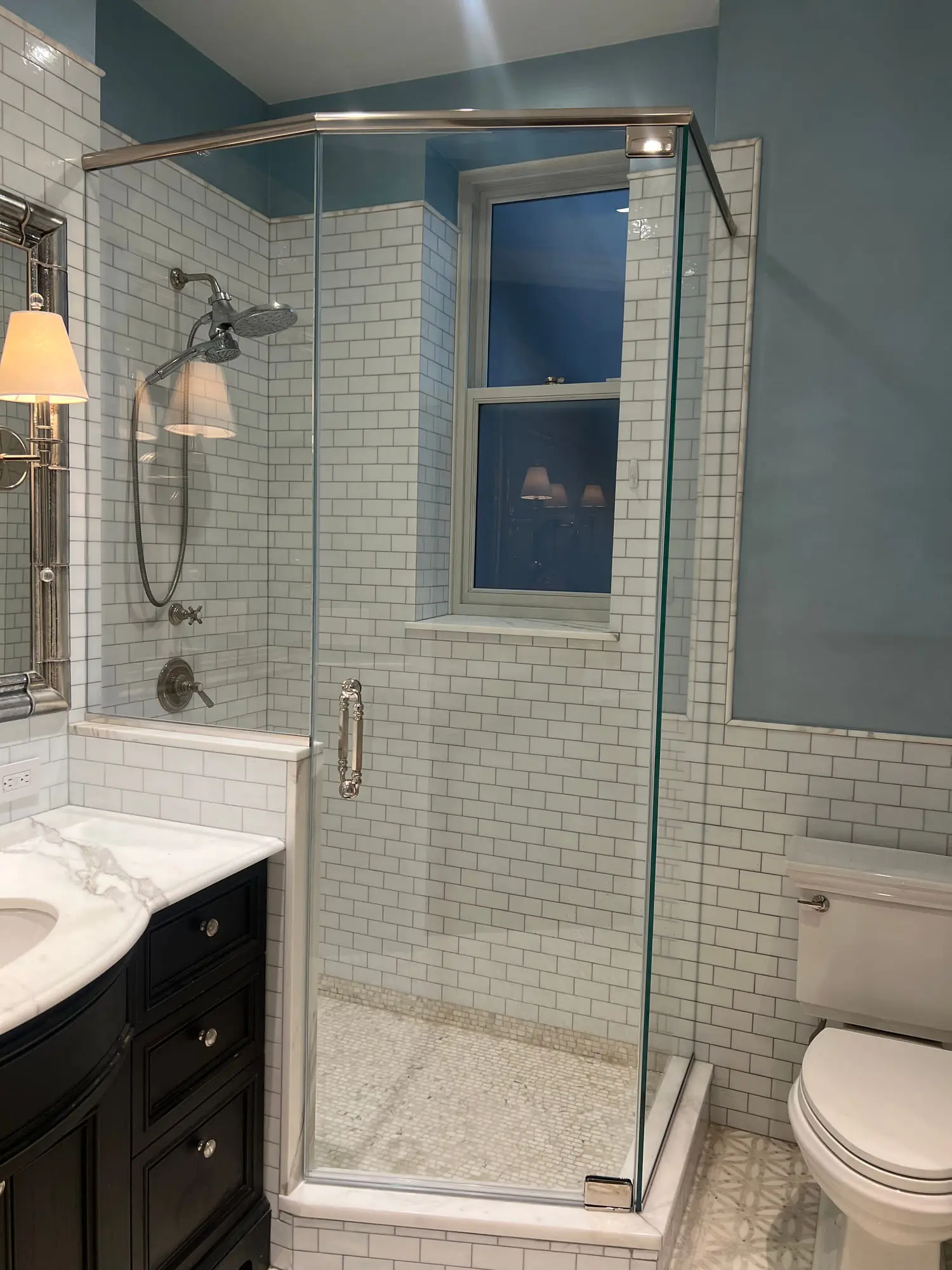 A neo-angle corner shower in white subway tile with a glass door, set against deep blue walls above a dark timber vanity