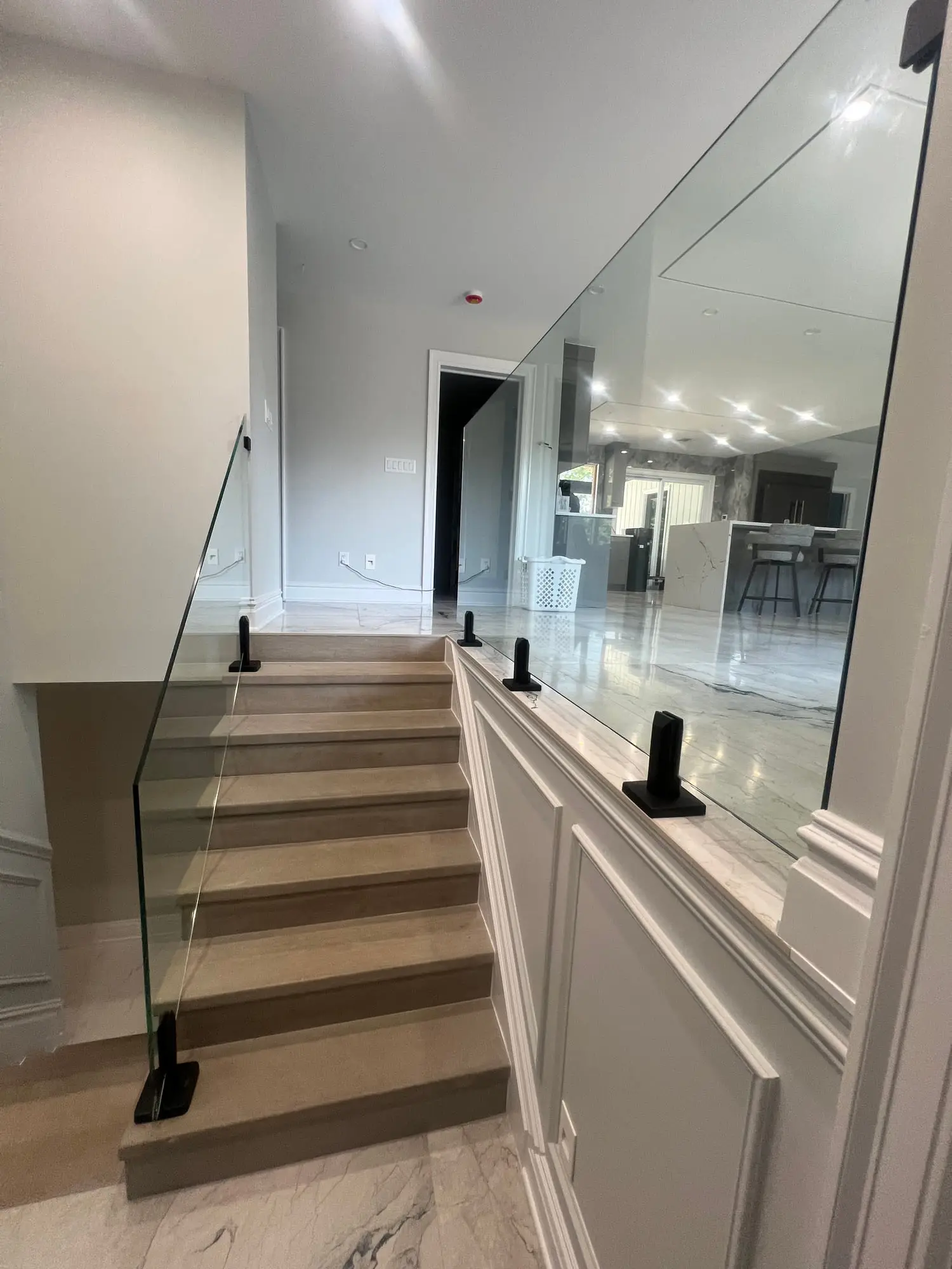 A glass railing with black standoff fittings running along a marble staircase and landing