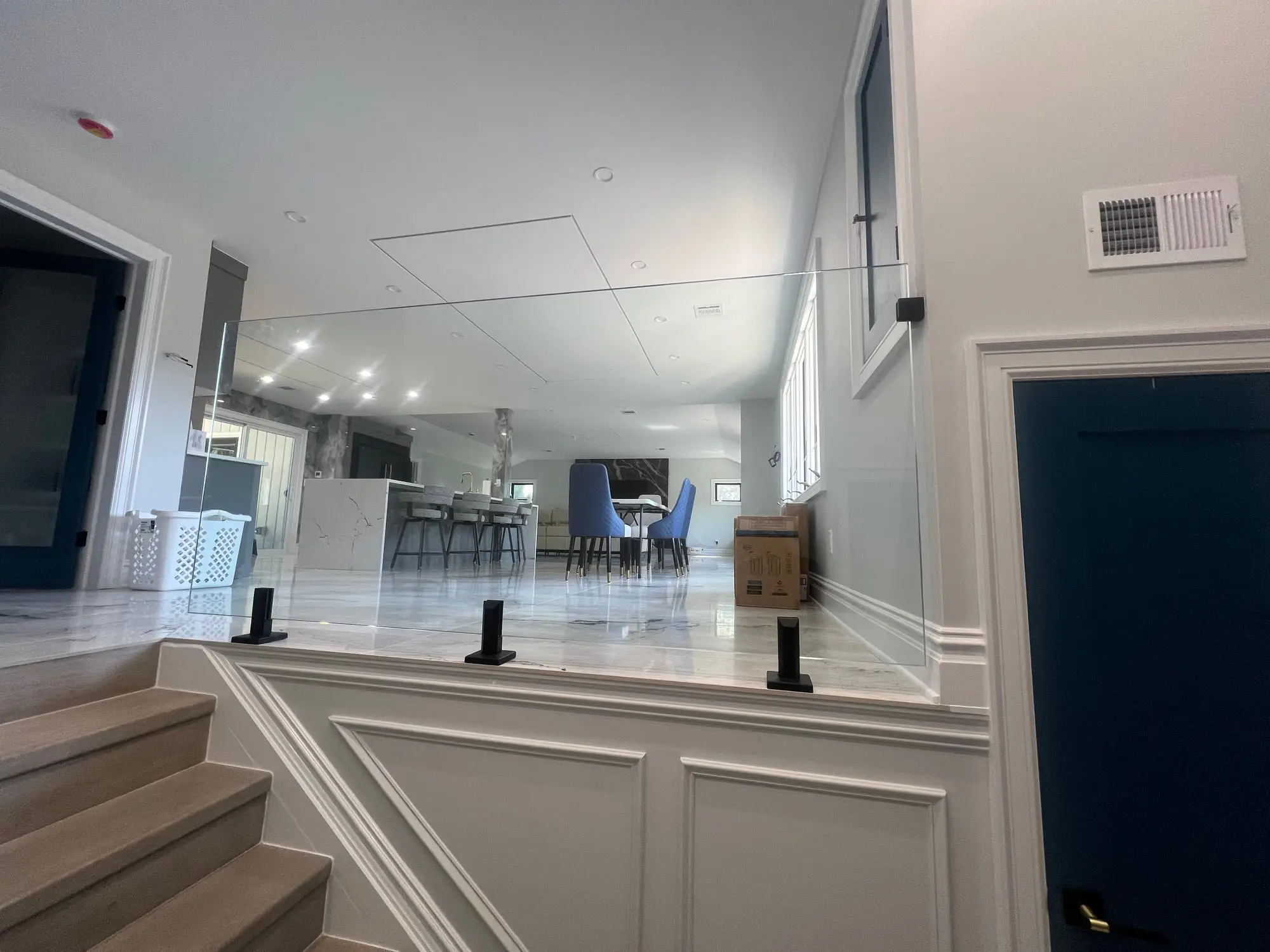 A frameless glass stair railing with black standoff fittings overlooking an open-plan kitchen and dining room