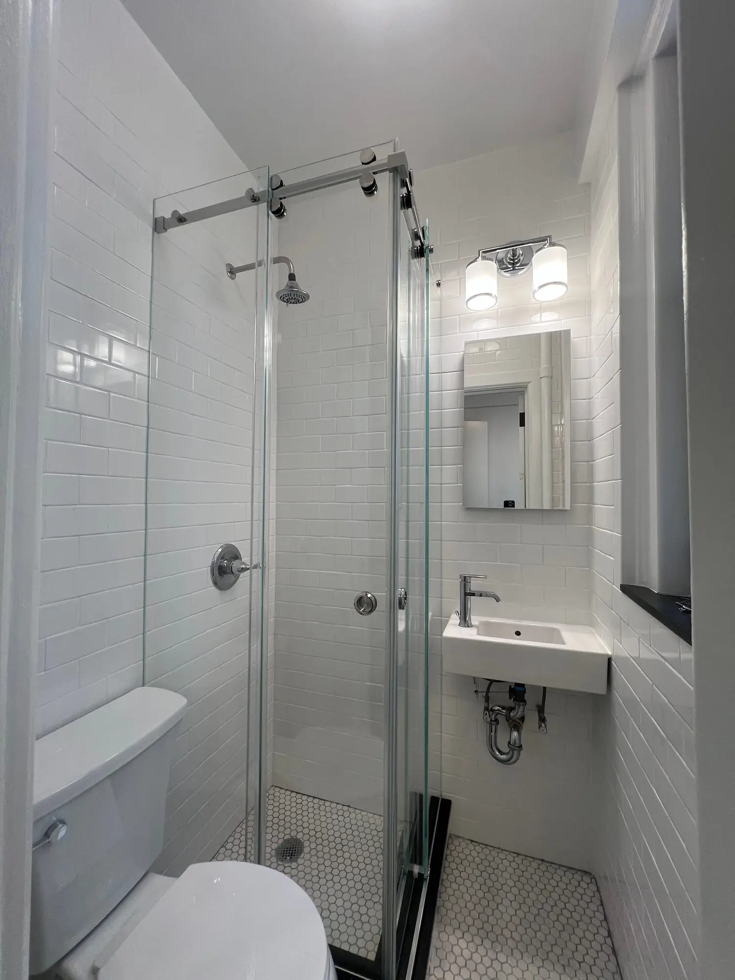 A white tiled shower with a sliding glass door on a black overhead rail