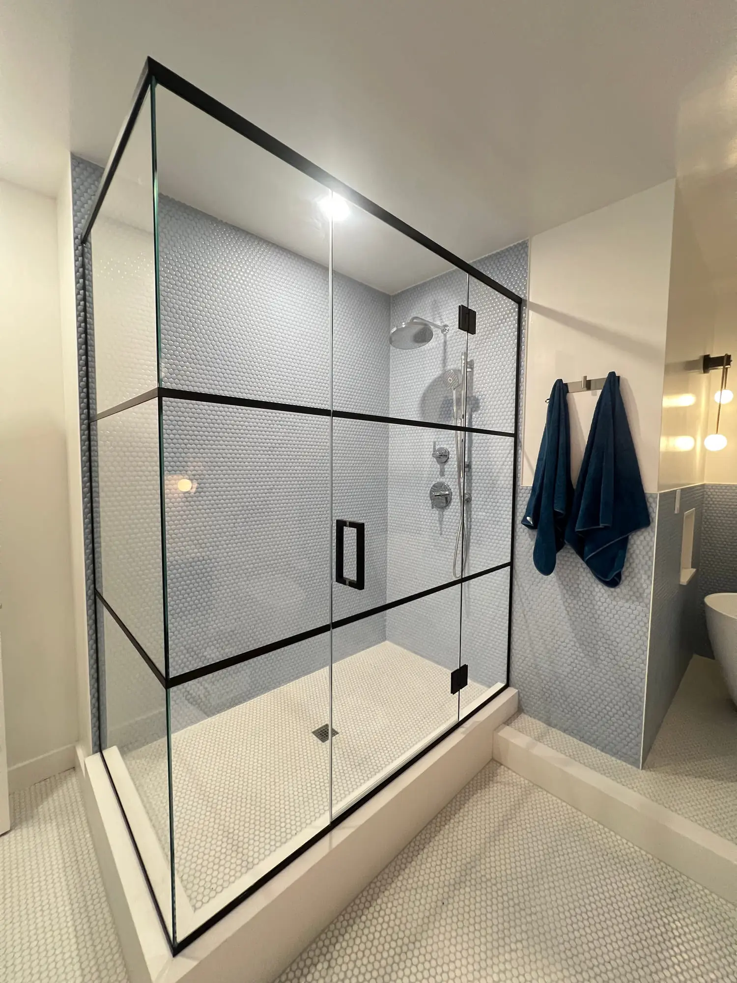 The black grid shower enclosure seen from the side, showing the return panel and door