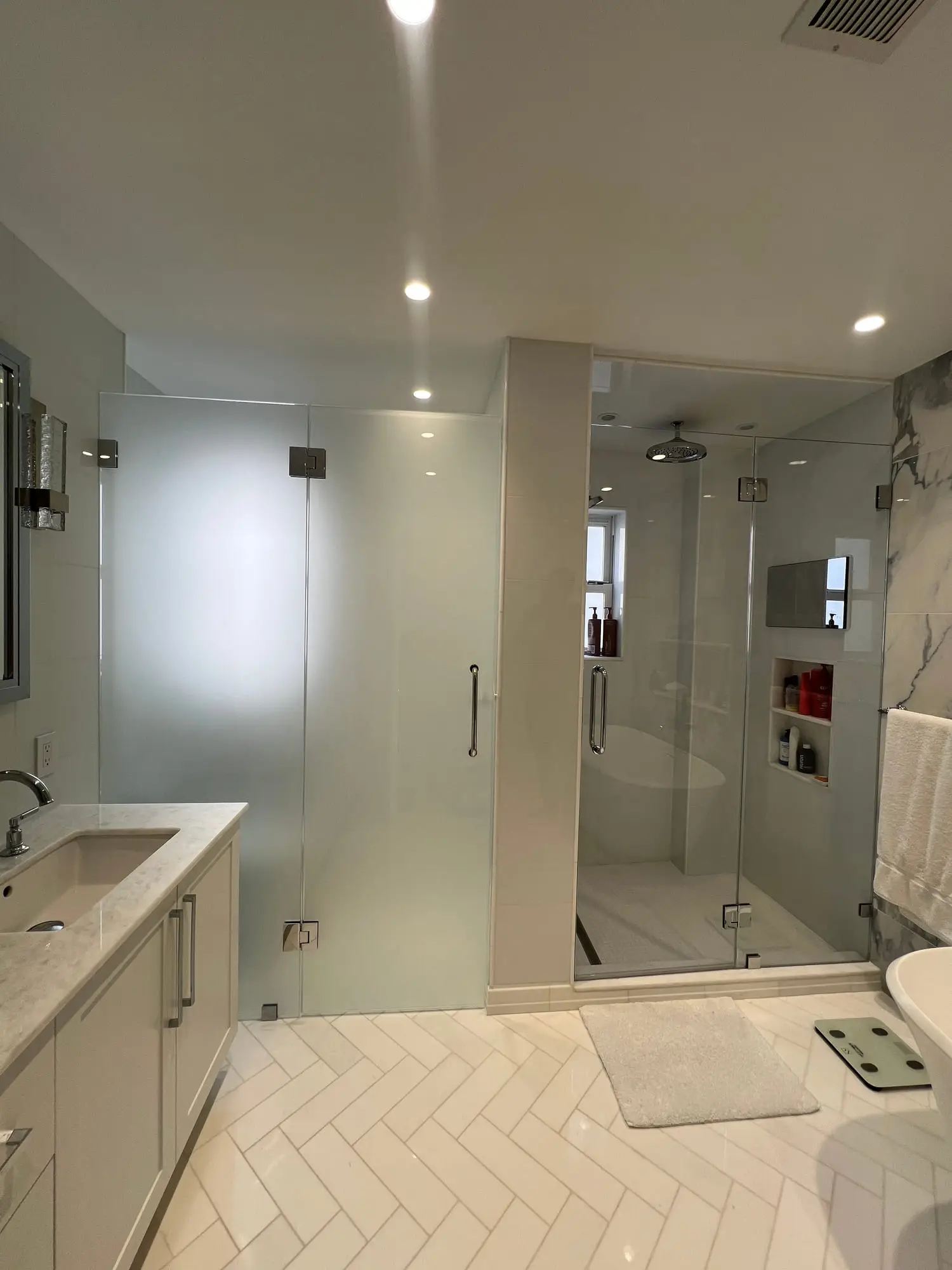 A shower door in fluted obscure glass opening onto a herringbone tiled floor and a white vanity