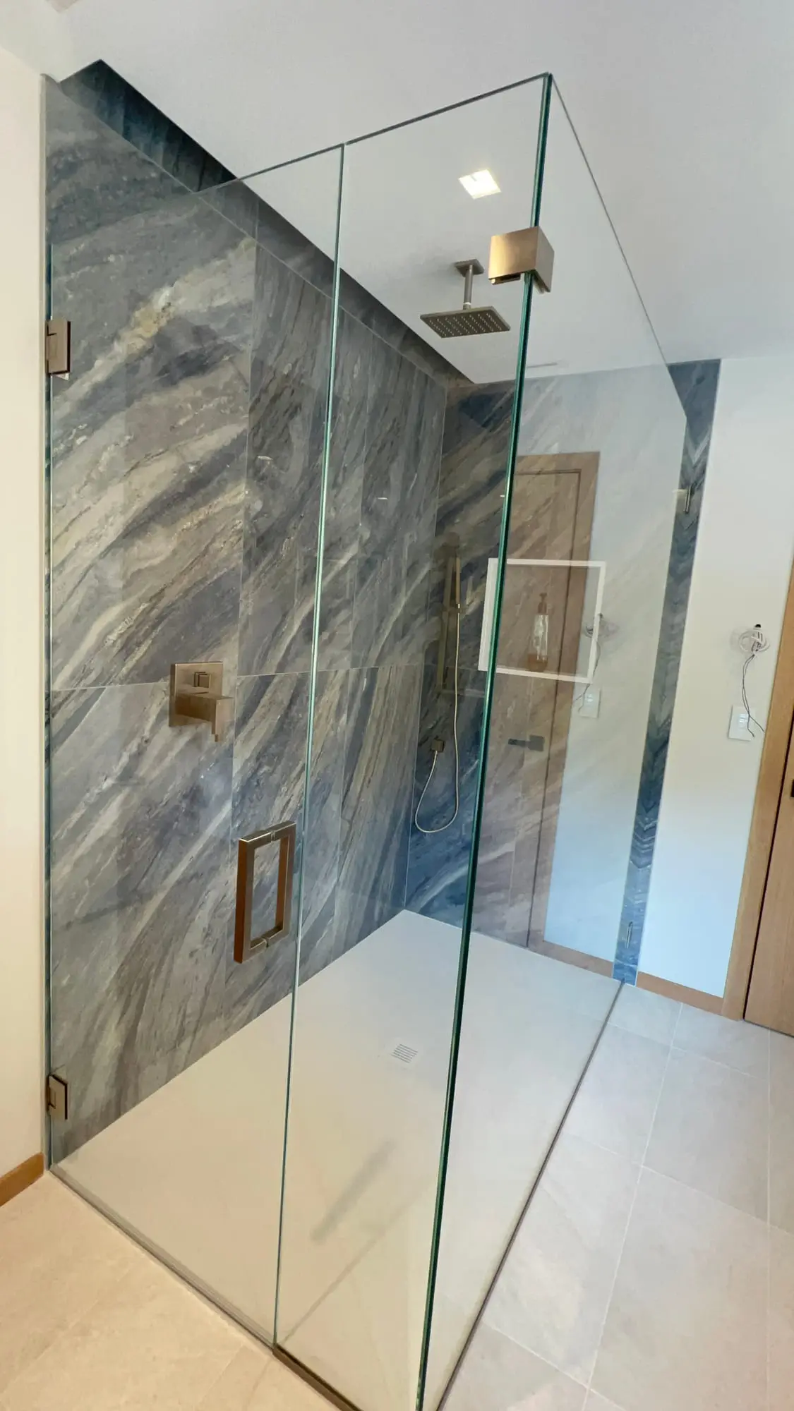 A frameless corner shower lined in blue-grey marble slab with brass fittings