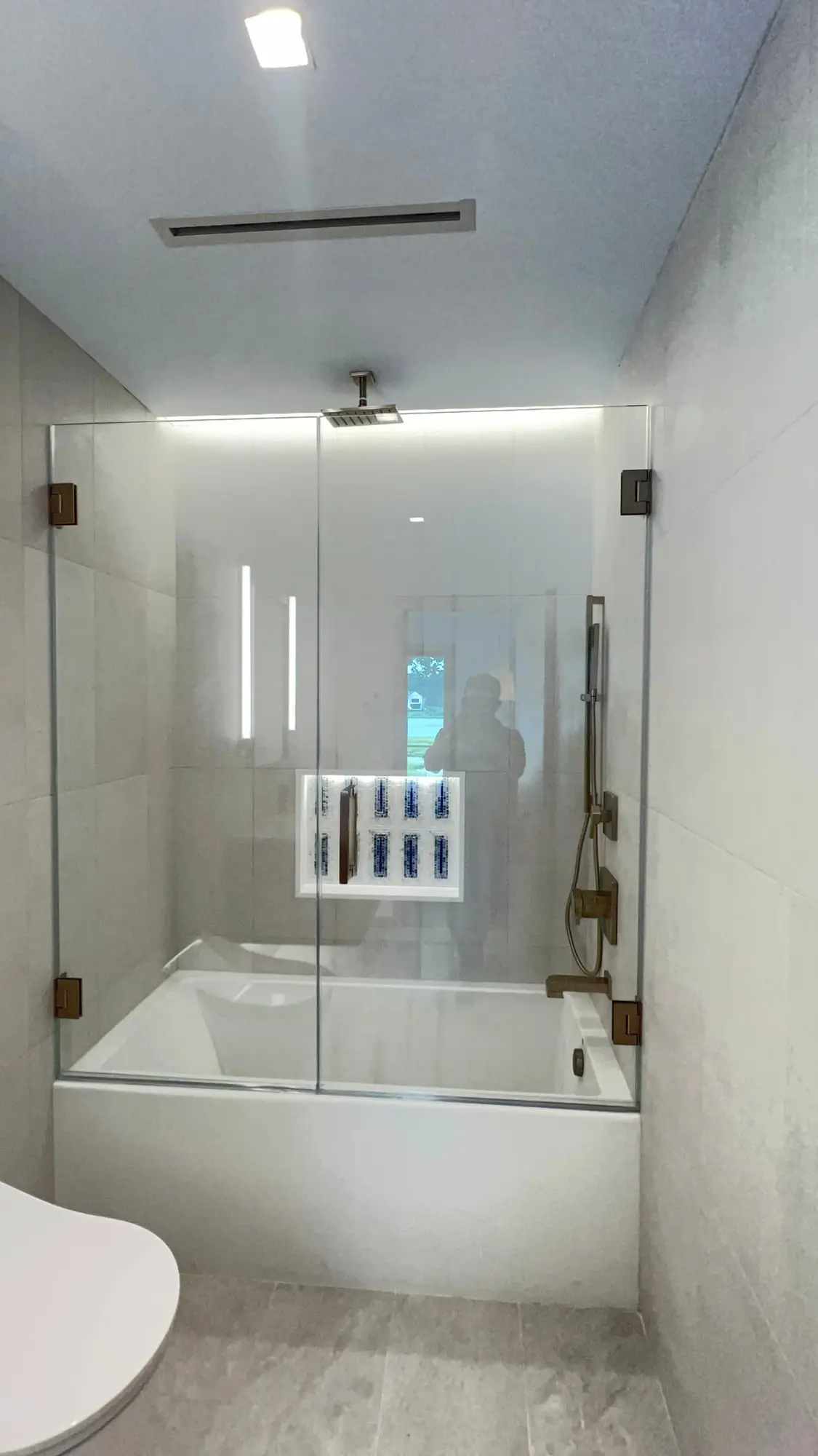 A frameless glass screen fitted to a curved soaking tub, with a gold rain head above
