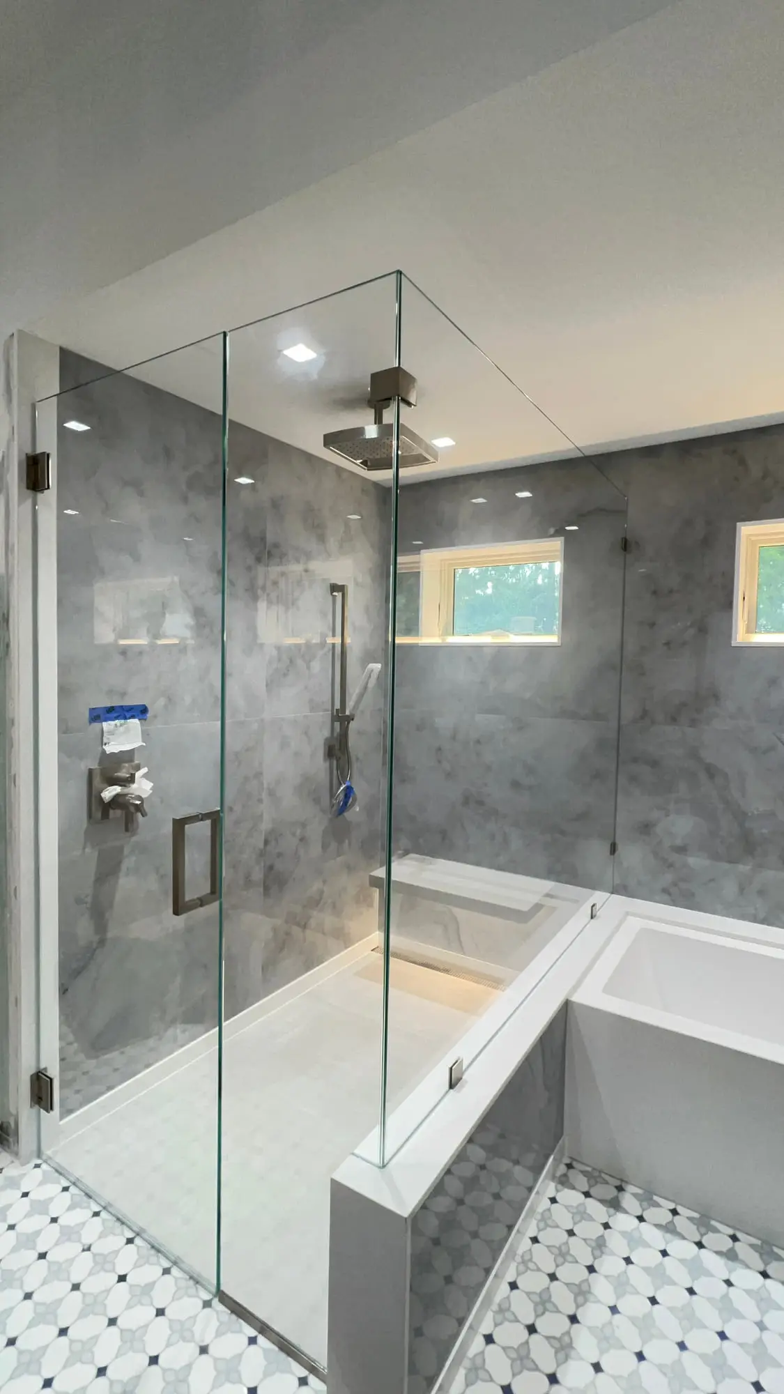 A frameless glass screen on a bath, with grey marble walls and a recessed shelf