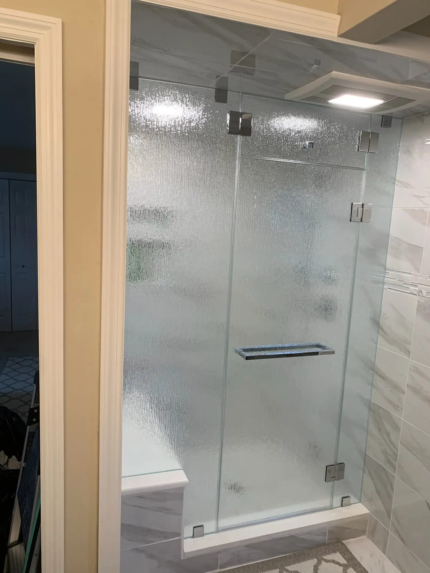 A shower door and panel in textured rain glass with chrome hinges and a towel bar, softening the view into the shower