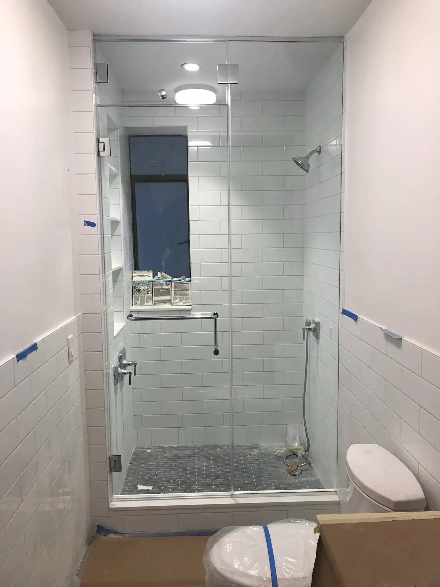 A frameless door between two fixed panels, enclosing a shower in white subway tile with a window at the back